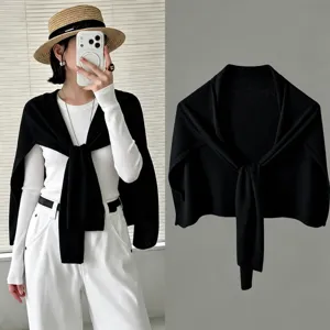 Vista detallada de un chal de punto negro liso, nudo elegante y diseño de hombros suave.