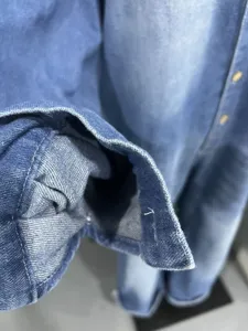 Close up detail view of women denim jumpsuit sleeve, vintage washed blue fabric texture.