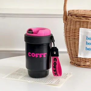 Close-up of a portable black travel coffee cup with pink lid and strap on white table.