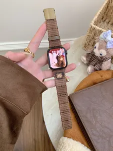 Brown corduroy watch band detail with cute bear charm and metal buckle for smartwatches.