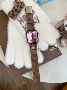 Brown corduroy Apple Watch strap detail showing cute bear embroidery and metal buckle design.