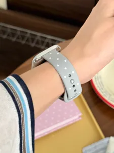 Primer plano de la correa de reloj de silicona gris con lunares usada en la muñeca.