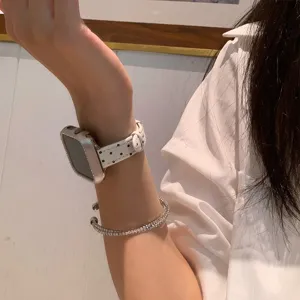 Detailopname van wit lederen horlogebandje met stippen gedragen om de pols met armband.