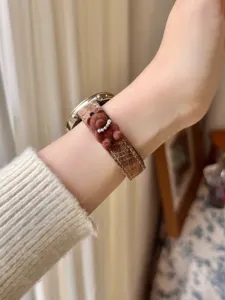 Close-up detail view of a stylish plaid watch strap featuring a cute 3D brown bear charm.