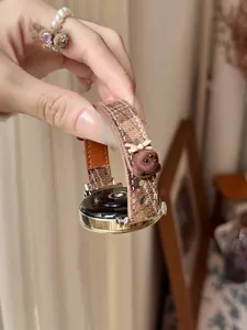 Close-up of stylish brown checkerboard smartwatch strap featuring cute bear charm.