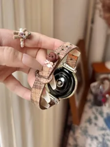 Close-up detail of brown plaid smartwatch strap featuring a cute 3D bear charm accessory.