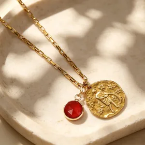 Gros plan détaillé du collier pendentif zodiaque doré avec charme en pierre rouge sur plateau.