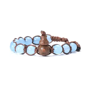 Gros plan d'un bracelet tressé avec des perles bleu clair et un pendentif en bois en forme de gourde.
