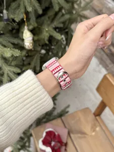 Close-up detail of a pink knitted winter pattern watch strap with metal buckle on a wrist.