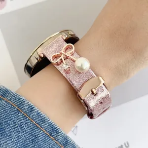 Detalle de correa de reloj inteligente con brillo rosa, lazo de oro rosa y abalorio de perla.