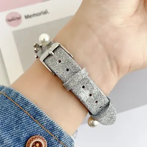 Detalle de correa de reloj con purpurina plateada, perlas elegantes y hebilla de metal.