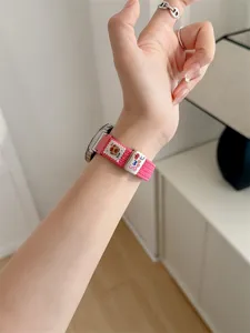 Close-up detail of the pink braided watch strap featuring a cute bear charm and sweet metal decor.