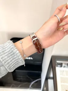 Detailaufnahme von braunem Lederuhrarmband mit elegantem Kleeblattarmband am Handgelenk.