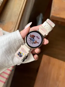 Détail du bracelet de montre en nylon tissé, sangle beige avec jolie boucle chat.