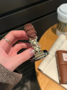 Gros plan détaillé du bracelet de montre en velours côtelé marron avec pendentifs perles et étoiles.