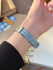 Detailansicht des blau-weiß gestreiften Jeans-Uhrenarmbands am Handgelenk getragen.