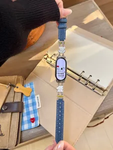 Nahaufnahme Detail des Jeans Smartwatch Armbands mit niedlichen weißen Hund Charms und blauem Design.