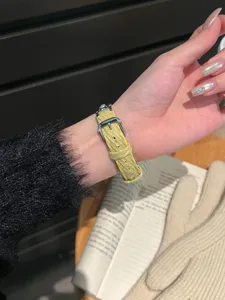 Vue détaillée d'un bracelet de montre en velours côtelé perlé porté au poignet avec livre.