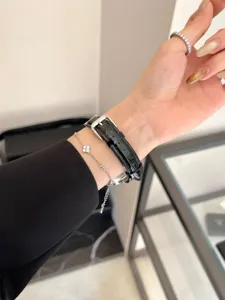 Handdetail mit schwarzem Lederuhrarmband und einem zarten silbernen Kleeblattarmband präsentiert.