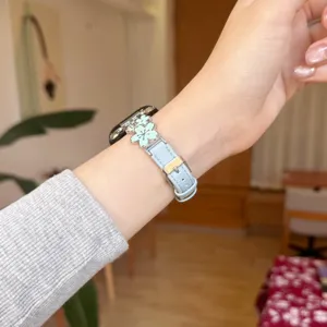 Close-up detail shot of light blue leather watch strap featuring metal flower charm.