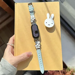 Close-up detail of metal flower leather watch band in light blue with delicate floral charms.