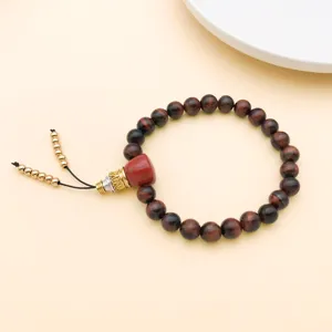 Nahaufnahme des DIY tibetischen Gebetsarmbands mit roten Perlen und Buddha-Kopf-Details.