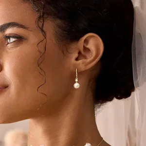 Close-up detail of elegant gold hoop earrings featuring a pearl drop and subtle rhinestone.