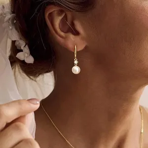 Close-up detail of elegant gold hoop earrings featuring sparkling crystal and a delicate white pearl.