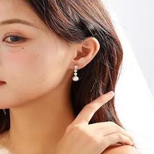 Dettaglio in primo piano di eleganti orecchini pendenti in oro 14k con perla e zirconi.