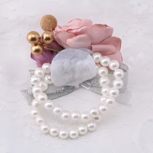 Elegant wedding wrist corsage detail with pink flower, gold beads, and pearl strands.