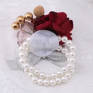 Close-up detail of wedding wrist corsage with pearls, red fabric flower and silver ribbon