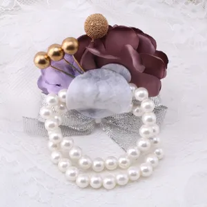 Close-up of elegant wedding wrist corsage with purple fabric flowers, pearls and silver ribbon.