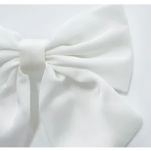 Gros plan détail d'une grande pince à cheveux nœud en satin blanc avec texture et beaux plis.
