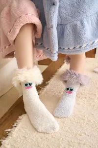 Gros plan détaillé de chaussettes moelleuses en polaire corail avec patchs de visages drôles.