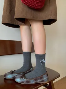 Dettaglio di calzini grigi in maglia con fiocco carino, perfetti per outfit quotidiani.
