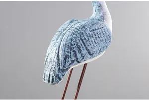 Close up of bird decor figurine with weathered blue texture and slim metal legs detail.