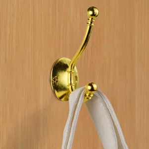 Detail view of a gold-finish double coat hook mounted on a wood background with a strap.