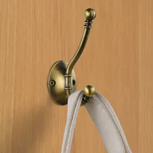 Detailed view of vintage brass coat hook mounted on wood wall, showing dual-head design.