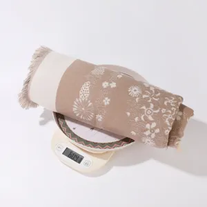 Detailed view of the winter tassel shawl roll, showing weight on scale and floral texture.