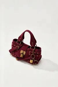 Dettaglio della borsa a tracolla in camoscio bordeaux con lucchetto in ottone e borchie.