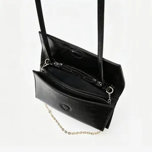 Vue détaillée du sac à bandoulière en cuir verni noir, montrant les compartiments et la chaîne.