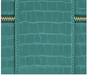Close-up detail of teal crocodile-textured leather handbag featuring precise stitching and gold zippers.