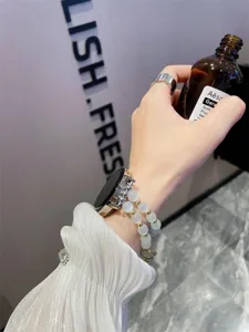 Detailopname van een elegante kralen smartwatch-band met kattenogen en metalen details.