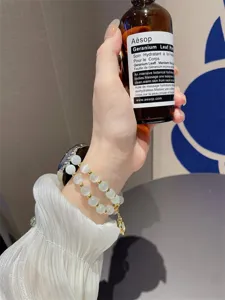 Detailopname van wit kattenoogsteen horlogebandje en kralenarmband met gouden metalen bedels.