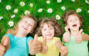 Children smiling on green grass with daisies outdoors lifestyle photography detail view.