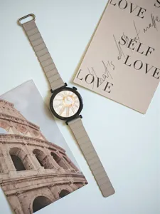 Elegante smartwatch con cassa nera, quadrante con numeri romani e cinturino in pelle grigia.
