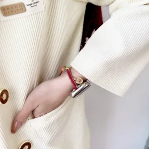 Red woven Apple Watch strap detail shot featuring lucky gold charms for autumn and winter.