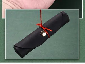 Closeup detail view of black soft leather storage pouch roll with red string and gold snap button.