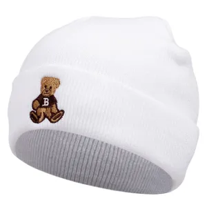 White knitted beanie with cute bear embroidery, winter warm wool hat detail shot, cozy style.