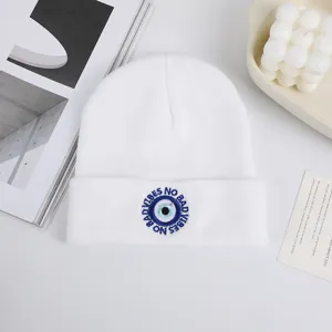 Dettaglio del berretto in maglia bianca con ricamo dell'occhio malvagio blu e design elegante.